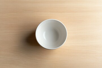 simple white ceramic bowl resting on light wooden tabletop perfectly centered with natural light casting soft shadows