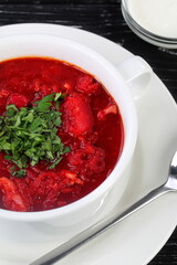 Traditional Ukrainian and Russian borscht in a white ceramic plate with herbs, sour cream and garlic on a black wooden background