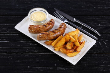 Sausages with potatoes and garlic sauce on a black background