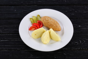 Cutlet with puree potatoes on a white plate on a black background