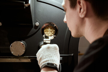 Male barista roasting green beans in the machine