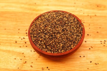 Crushed Black Pepper (Piper nigrum L, in a wooden bowl and some scattered, seen from above with close up view.
