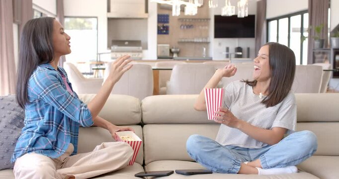 Eating popcorn and chatting, two teenage girls hanging out on couch