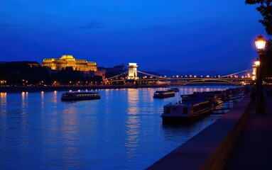 Nighttime view of a city with illuminated buildings, bridge and boats on river