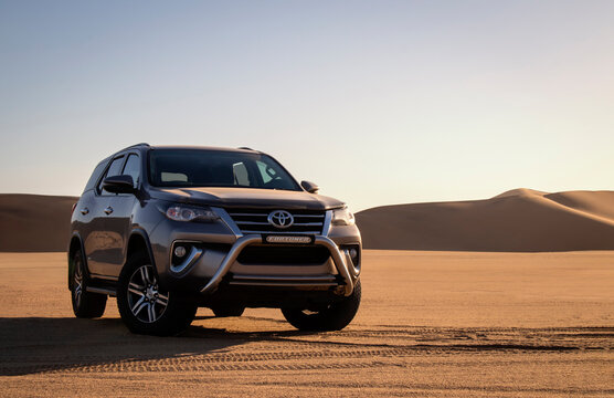 A gray Toyota Fortuner in the middle of the Namib Desert against a bright sky
