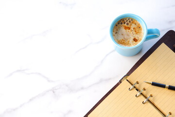 ミルクをたっぷり入れたコーヒー、カフェ・ラッテを飲みながら、システム手帳でデスクワークをしているイメージの写真素材
