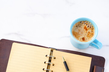 ミルクをたっぷり入れたコーヒー、カフェ・ラッテを飲みながら、システム手帳でデスクワークをしているイメージの写真素材
