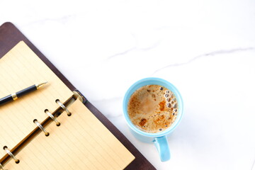 ミルクをたっぷり入れたコーヒー、カフェ・ラッテを飲みながら、システム手帳でデスクワークをしているイメージの写真素材
