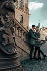 Fototapeta premium couple standing next to stone stairs on the street. A man and a woman hug and look at each other with a smile.