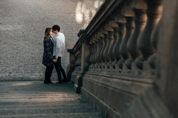 couple standing next to stone stairs on the street. A man and a woman hug and look at each other with a smile.