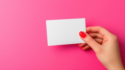 Obraz premium A hand with red nail polish holds a blank card against a bright pink background, creating a vibrant and eye-catching composition.