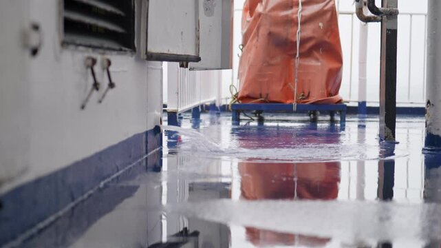 Rainwater draining from a scupper onto the ship&rsquo;s wet deck; static low-angle shot