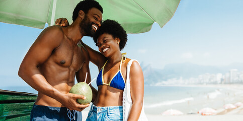 Joyful African couple enjoying Ipanema Beach under sun umbrella