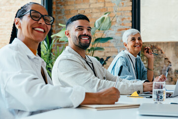 Smiling business professionals taking notes during a collaborative meeting in a sunlit office with...
