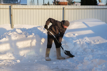 A man in felt boots clears snow in the backyard with a shovel