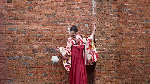 A young woman in her 20s wears a traditional graduation ceremony Hakama (kimono) in Japan and stands in a traditional Japanese brick building.