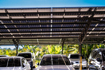 Naklejka premium Engineer in safety vest and helmet pointing towards a solar powered carport, illustrating eco-friendly innovation in parking infrastructure. Solar panels provide shade and sustainable energy.