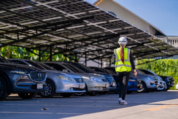 Engineer in safety vest and helmet pointing towards a solar powered carport, illustrating eco-friendly innovation in parking infrastructure. Solar panels provide shade and sustainable energy.