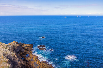 Rocky coast with sailboats at the horizon on a blue sea