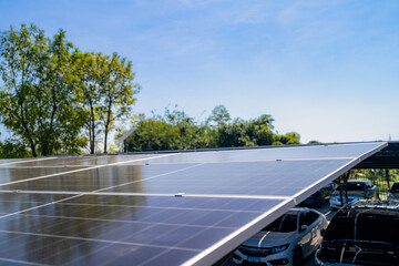 Close up view of solar panels installed on a carport with trees and parked cars under a clear blue sky. Showcasing renewable energy, sustainability, and efficient solar power systems for clean energy. © ultramansk