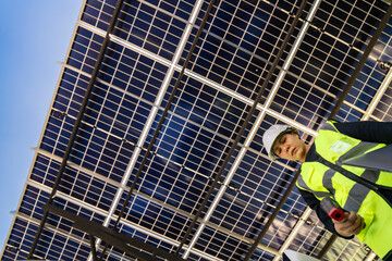 Technician inspects solar panels under a large solar carport structure. Focused on clean energy,...