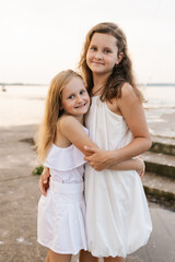 Two young girls are standing on beach, smiling and hugging each other