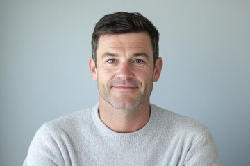 Fototapeta premium A middle-aged man with short brown hair, wearing a grey sweater, smiles gently at the camera.