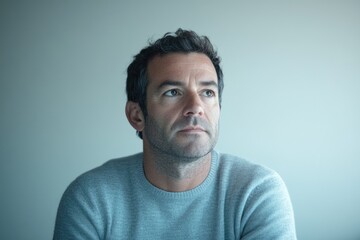 A pensive middle-aged man with short, dark hair gazes thoughtfully into the distance.