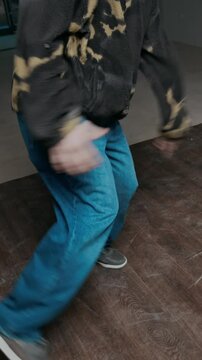 Vertical handheld shot of talented Caucasian gen Z b-boy in streetwear improvising breakdance while performing creative top rock moves indoors