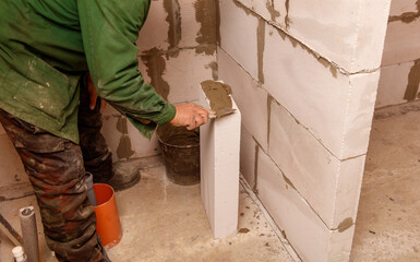 A man is working on a wall, using a trowel to spread mortar
