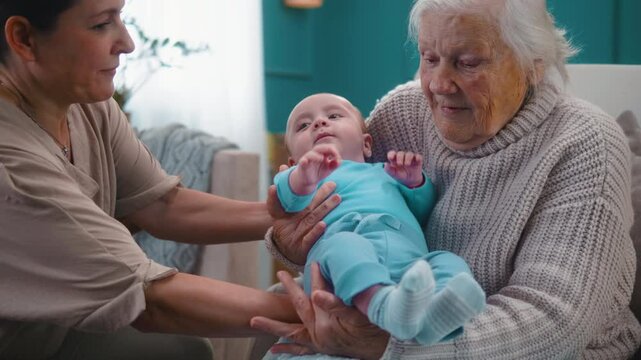 An excited 80s grandmother holds her newborn grandson for the first time from her adult daughter. three generations together
