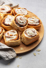 Delicious cinnamon rolls with white icing and almond flakes resting on wooden plate
