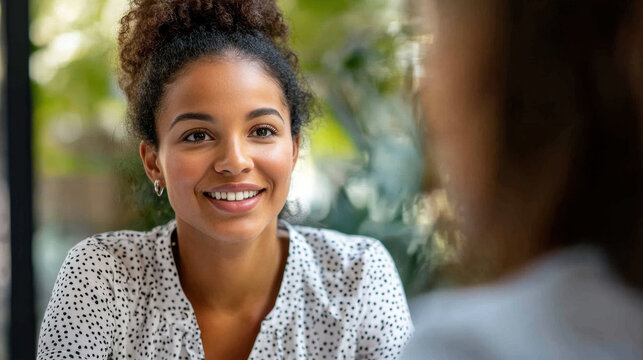 Smiling woman with curly hair engaging in conversation, showcasing friendly atmosphere and connection. background features greenery, enhancing warm vibe