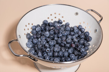 Freshly washed blueberries in metal strainer on light background, highlighting freshness and naturalness. Concept of healthy eating, food and freshness
