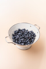 Metallic white strainer with freshly washed blueberries on light background, highlighting freshness and naturalness. Concept of healthy eating, food and freshness