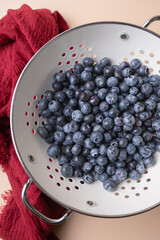 Fresh blueberries in white colander with red cloth detail on light background, highlighting freshness and rustic style. Concept of natural cooking and healthy eating