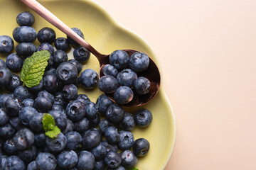 Close-up of fresh blueberries on light green plate and copper spoon, decorated with mint leaves and beige background. Healthy eating concept