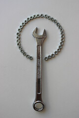 Drop forged spanner inside a circular pattern of steel nuts similar to a hand magnifying glass
