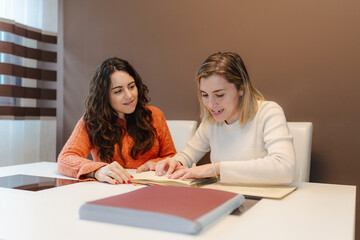 Blind woman reading a Braille book while sharing the experience with her friend, promoting...