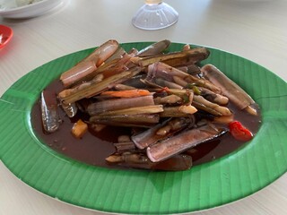 A Chinese Dish Bamboo clams steamed in sweet and sour sauce garnished with Spring Onions and Fried Garlic on green plate
