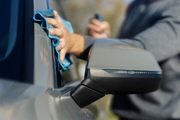 Close up of man's hand rubbing his car with microfiber cloth at car wash.