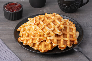 Delicious waffles topped with strawberry jam on a black plate with a grey wooden background