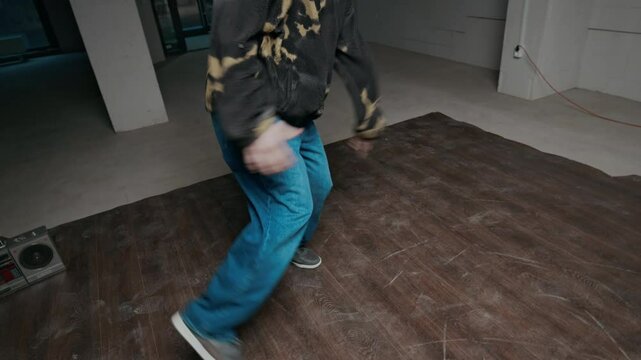 Handheld shot of talented Caucasian gen Z b-boy in streetwear improvising to music break dancing indoors and performing creative top rock moves