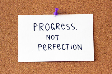 Cork notice board with a push pin paper sign that says 'progression, not perfection'