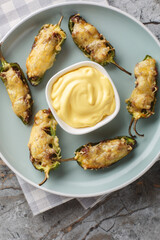 Homemade Organic Jalapeno Poppers with ground meat and cheese served with cheese sauce closeup on the plate on the table. Vertical top view from above
