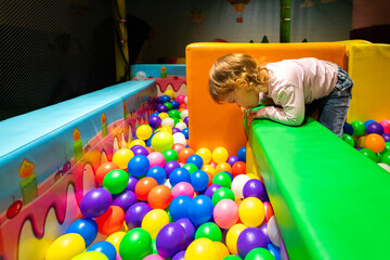 A curious child leaning over a soft structure observing colorful balls in a vibrant play area.