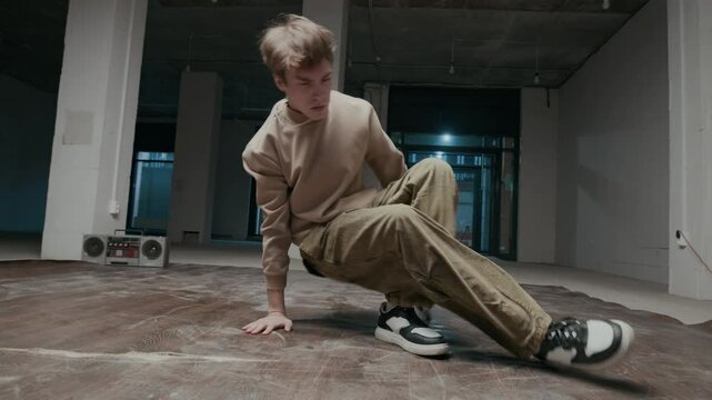 Ground level shot of talented Caucasian male zoomer in streetwear performing down rock moves showing his creative individuality while break dancing indoors