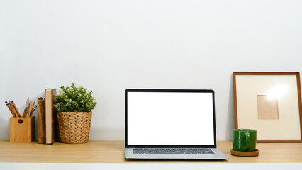 Fototapeta premium Minimalist workspace with blank screen laptop, a green coffee mug and potted plant