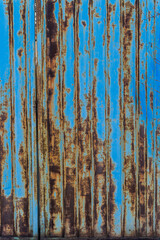 A close-up view of a blue metal gate weathered with rust, showcasing vertical streaks of corrosion and fading paint. The rich textures and earthy colors create an artistic contrast 