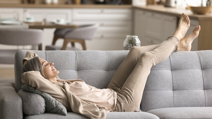 Peace of mind. Smiling tranquil mid aged woman take time to relax on comfy couch give tired legs a...